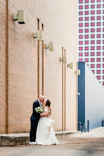 a bride and groom kissing in front of a brick building