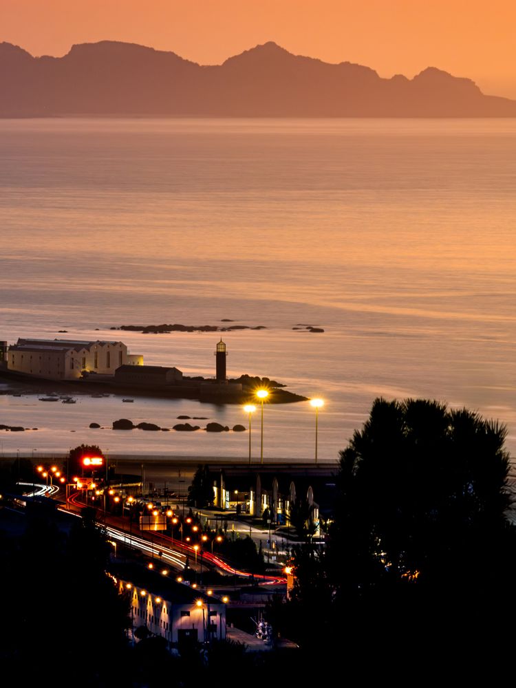 A view of the ocean at dusk with a lighthouse in the distance