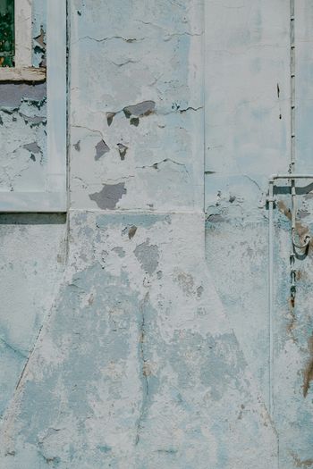 a wall with peeling paint and a window