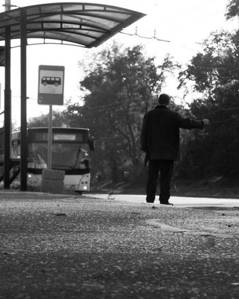 a black and white photo of a man waiting at a bus stop