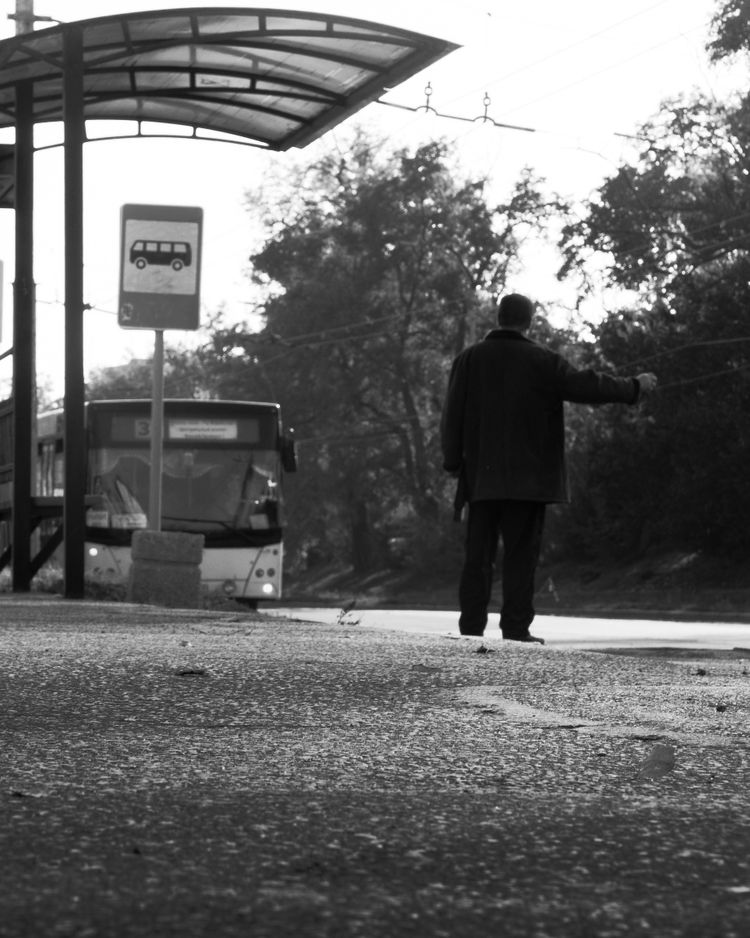 a black and white photo of a man waiting at a bus stop