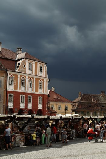 A crowd of people standing around a market under a cloudy sky