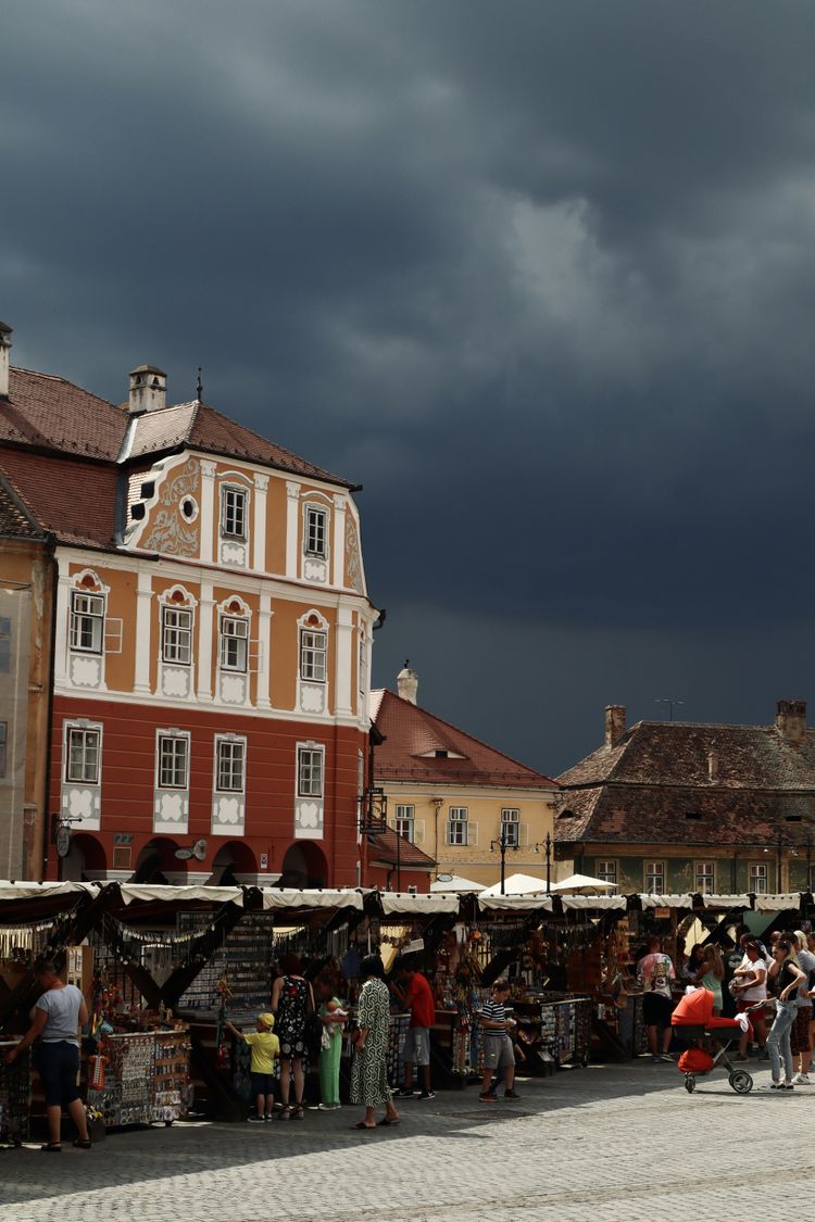 A crowd of people standing around a market under a cloudy sky
